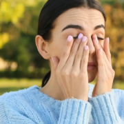 Donna con sintomi di allergia primaverile Donna all’aperto che si strofina gli occhi per prurito dovuto ad allergie primaverili, con sfondo di alberi e erba.